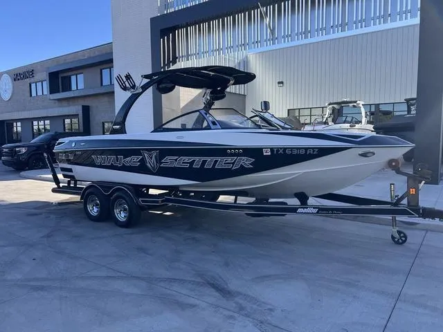 Slide: The Image of 2009 Malibu Wakesetter 23 LSV boat on trailer, parked outside a modern building. - 2
