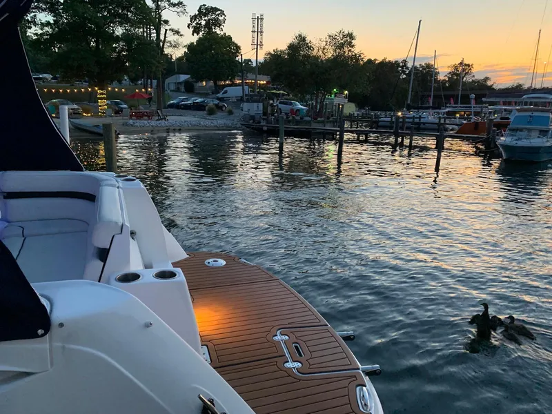 Slide: The Image of 2018 Rinker EX 270 boat docked at sunset, with calm waters and nearby marina. - 10