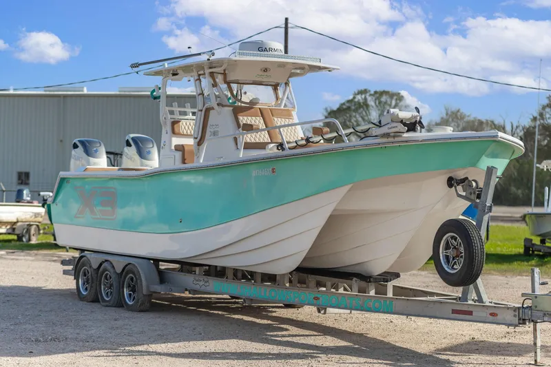 Slide: The Image of 2019 Shallow Sport 32 X3 boat on trailer, turquoise hull, dual engines, sunny day. - 4