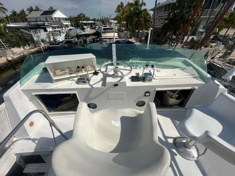 Slide: The Image of 1974 Bertram 42 Motor Yacht helm with steering wheel, controls, and seating, docked near palm trees. - 16