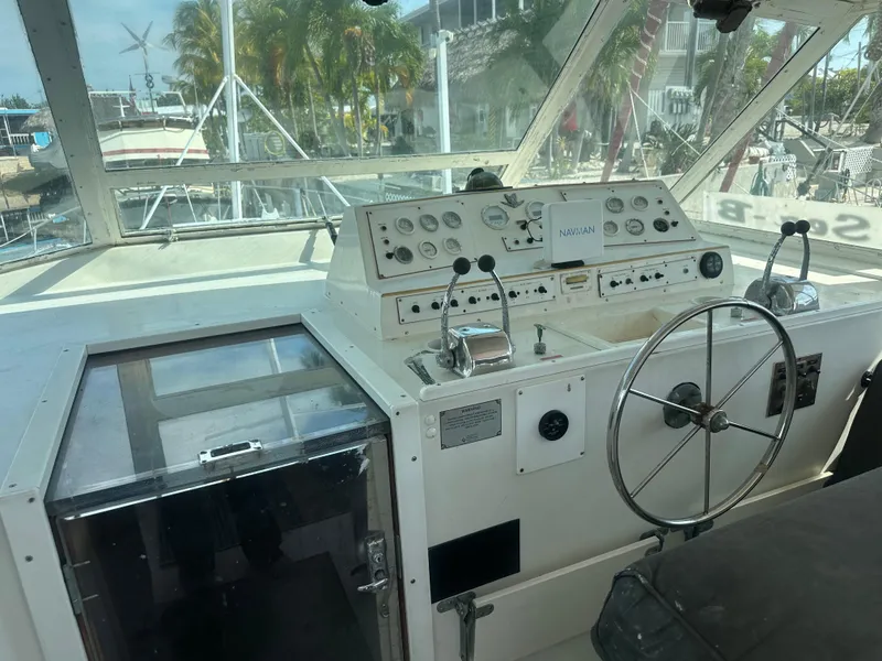 Slide: The Image of 1974 Bertram 42 Motor Yacht helm with steering wheel and control panel, docked at marina. - 24