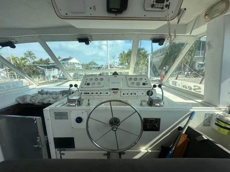 Slide: The Image of 1974 Bertram 42 Motor Yacht helm with steering wheel and control panel, docked in a marina. - 25