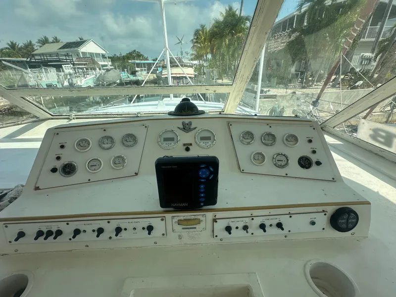 Slide: The Image of 1974 Bertram 42 Motor Yacht dashboard with gauges and controls, docked near palm trees. - 26