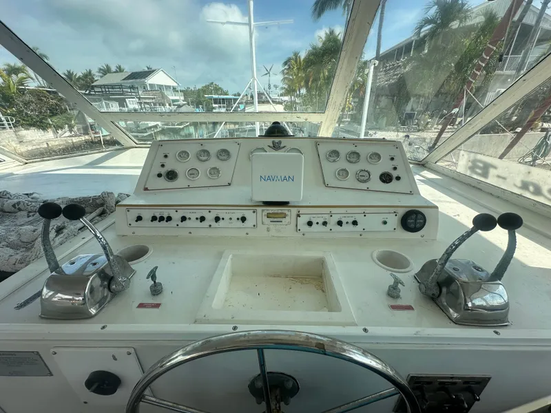 Slide: The Image of 1974 Bertram 42 Motor Yacht helm with controls and gauges, docked near palm trees. - 28