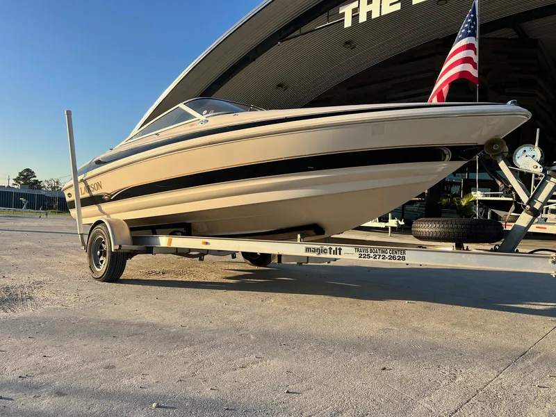 Slide: The Image of 2002 Larson LXi 190 boat on trailer with American flag, parked outside a building. - 5