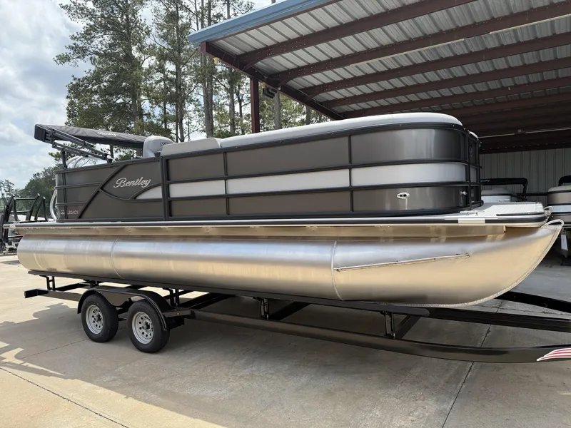 Slide: The Image of 2025 Bentley Pontoons Legacy Cruise XL 220 on trailer, parked under a metal canopy. - 1
