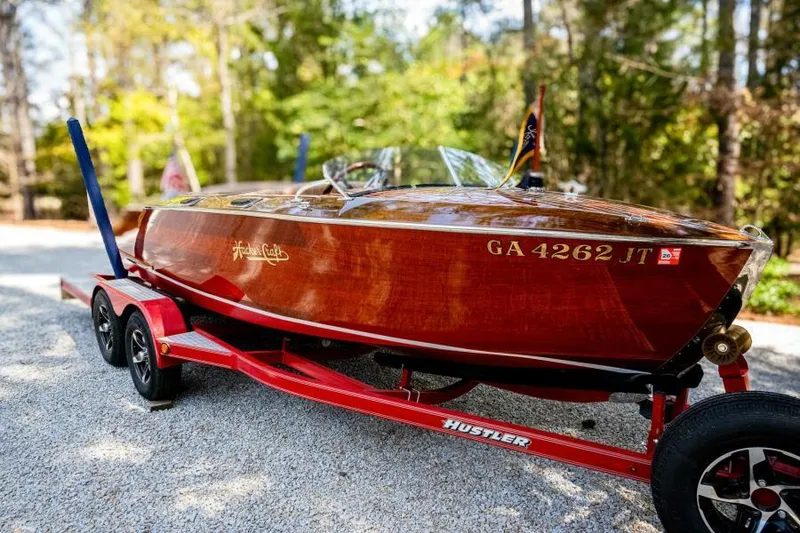 The Image of 1941 Hacker-Craft Deluxe boat on red trailer, surrounded by trees. - 0