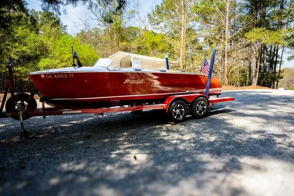 Slide: The Image of 1941 Hacker-Craft Deluxe boat on trailer, surrounded by trees, with American flag. - 11