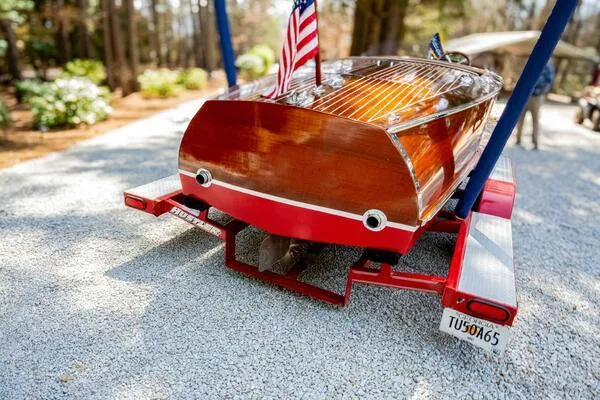Slide: The Image of 1941 Hacker-Craft Deluxe boat on trailer, American flag, parked on gravel driveway. - 22