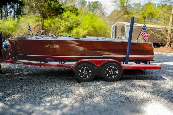 Slide: The Image of 1941 Hacker-Craft Deluxe boat on trailer with American flags, surrounded by trees. - 29