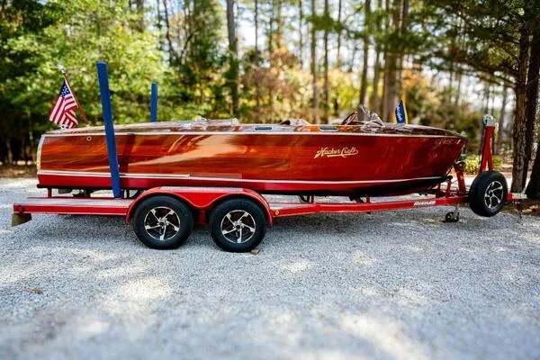 Slide: The Image of 1941 Hacker-Craft Deluxe boat on a red trailer, surrounded by trees. - 47