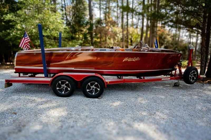 Slide: The Image of 1941 Hacker-Craft Deluxe boat on red trailer, surrounded by trees. - 8