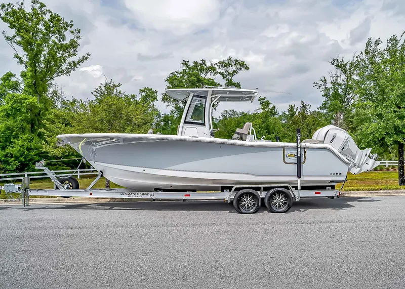Slide: The Image of 2025 Sea Hunt Ultra 275 SE boat on trailer, parked on road with trees in background. - 2