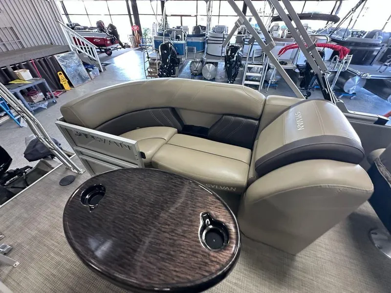 Slide: The Image of 2022 Sylvan 8522 Mirage LZ pontoon boat interior with beige seating and wooden table. - 11