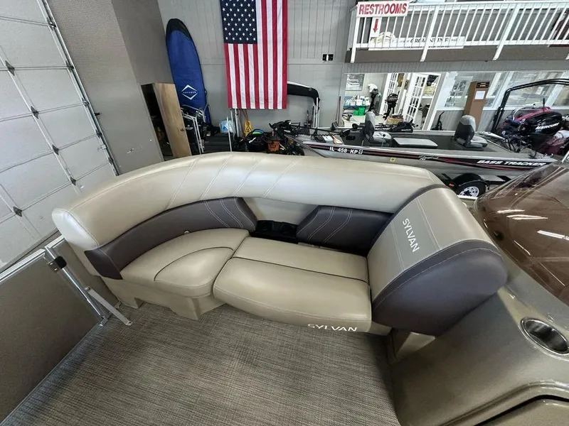 Slide: The Image of 2022 Sylvan 8522 Mirage LZ boat interior with beige seating and American flag backdrop. - 3