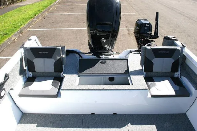 Slide: The Image of 2023 Crestliner 1700 Vision boat interior with seating and motor, parked on pavement. - 12