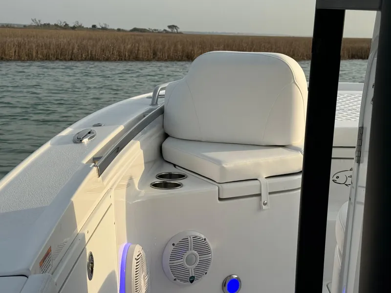 Slide: The Image of 2025 Crevalle 24 HCO boat interior with white seating, cup holders, and speaker on calm water. - 12