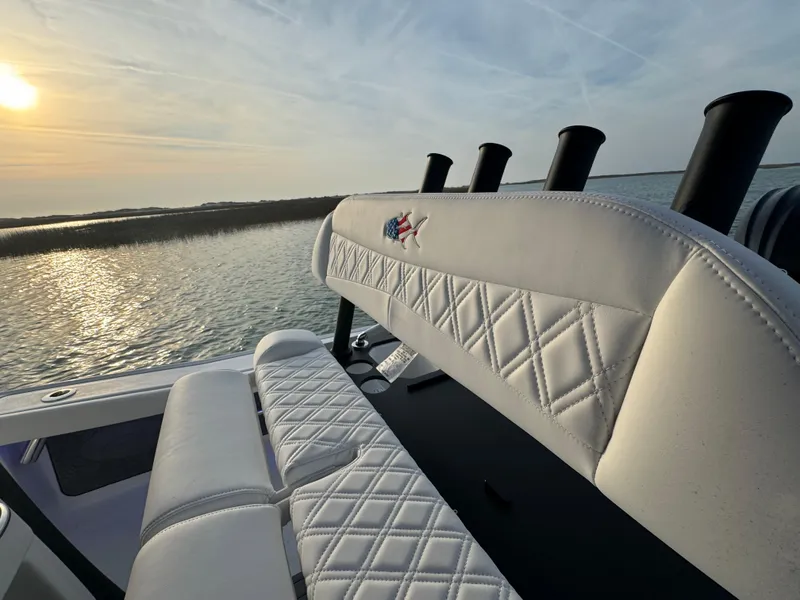 Slide: The Image of 2025 Crevalle 24 HCO boat with white diamond-stitched seating, overlooking serene water at sunset. - 33