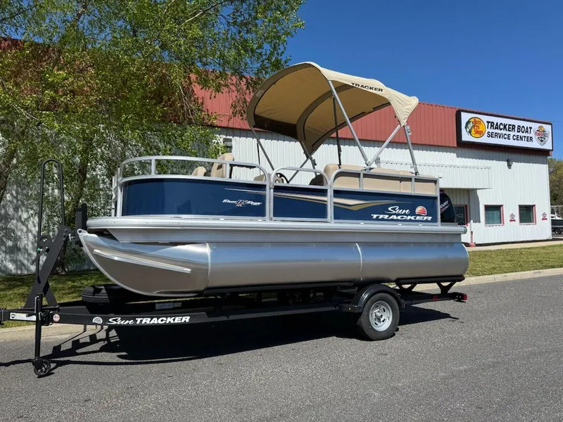 Slide: The Image of 2025 Sun Tracker Bass Buggy 16 XL Select pontoon boat on trailer, outside service center. - 3