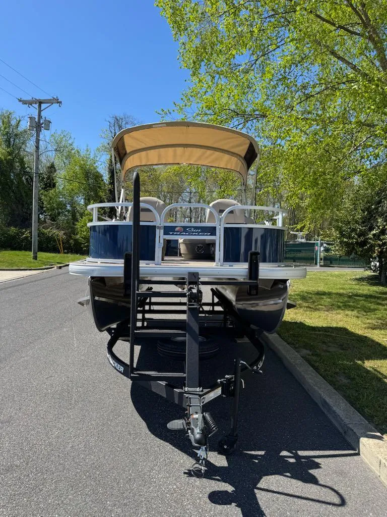 Slide: The Image of 2025 Sun Tracker Bass Buggy 16 XL Select pontoon boat on trailer, parked on a sunny street. - 4