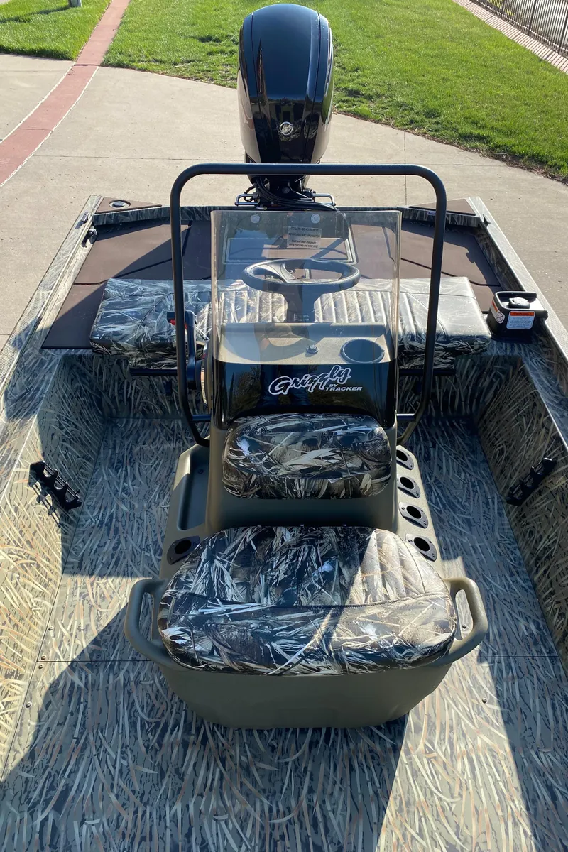 Slide: The Image of 2025 Tracker Grizzly 1860 CC boat with camouflage seating and console, parked on concrete. - 4