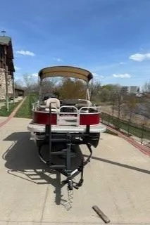 Slide: The Image of 2025 Sun Tracker Bass Buggy 16 XL Select pontoon boat on trailer, outdoors. - 2