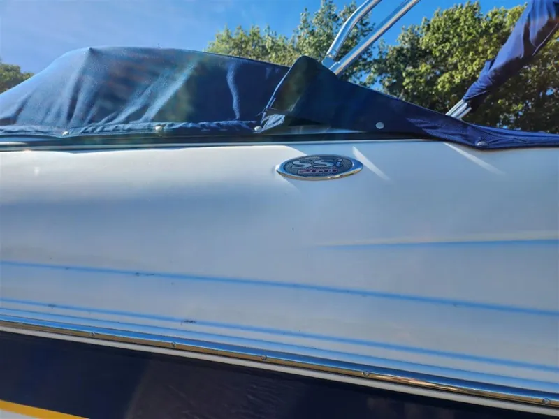 Slide: The Image of 2003 Chaparral 260 SSi boat with blue cover and emblem, under clear sky. - 13