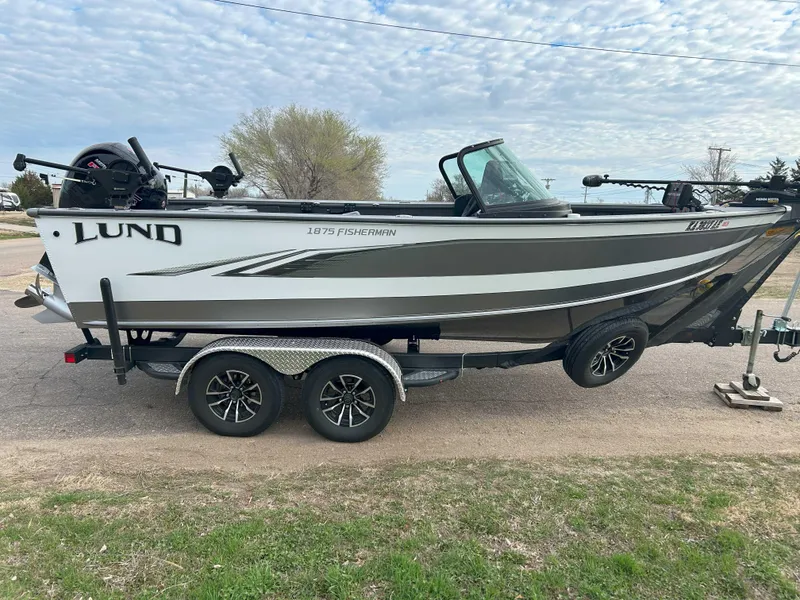 Slide: The Image of 2024 Lund 1875 Fisherman boat on trailer, parked outdoors under cloudy sky. - 4
