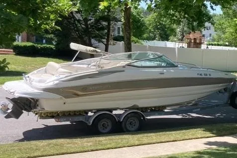 The Image of 2006 Crownline 262 EX boat on trailer, parked on a sunny residential street. - 0