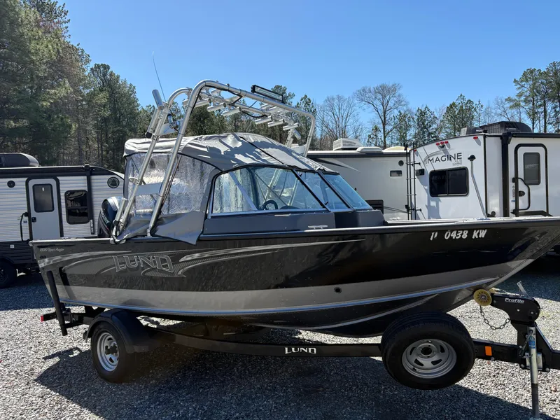 Slide: The Image of 2017 Lund 1800 Sport Angler boat on trailer, parked near RVs and trees. - 5