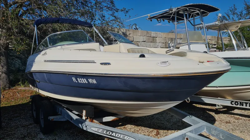 The Image of 2005 Sea Ray 200 Sundeck boat on trailer, parked outdoors under clear blue sky. - 0