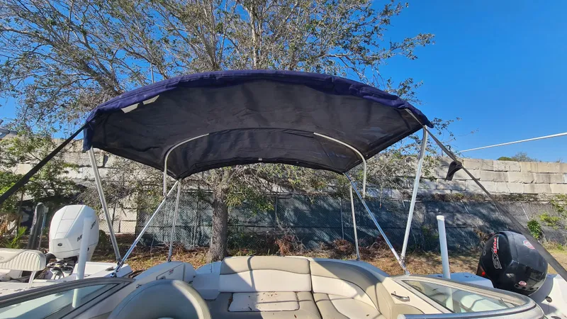 Slide: The Image of 2005 Sea Ray 200 Sundeck boat with canopy, parked outdoors under clear blue sky. - 12