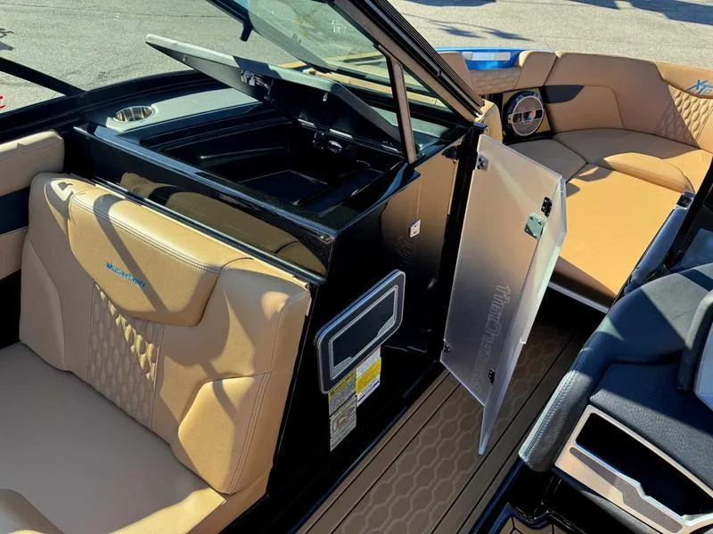 Slide: The Image of 2022 MasterCraft XT23 boat interior with tan seating and open storage compartment. - 2