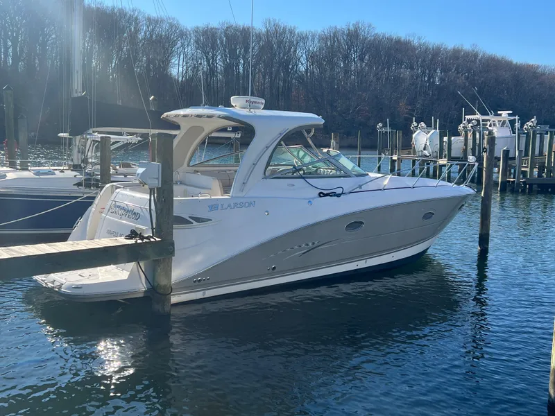 Slide: The Image of 2007 Larson Cabrio 350 boat docked in a marina, surrounded by calm water and trees. - 0