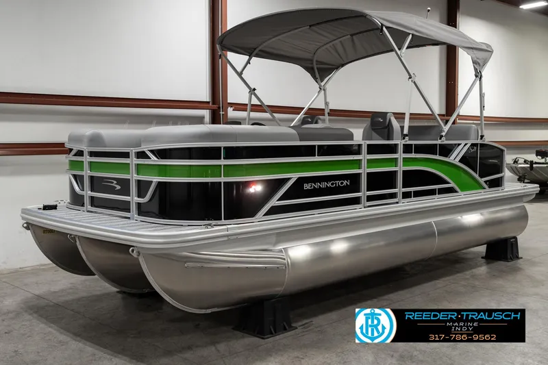 Slide: The Image of 2025 Bennington 21 SSB pontoon boat with green accents in a showroom. - 2