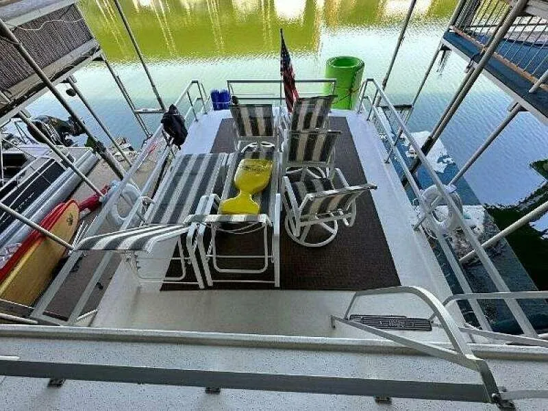 Slide: The Image of 2004 Gibson 50 Houseboat deck with striped chairs and table by the water. - 18