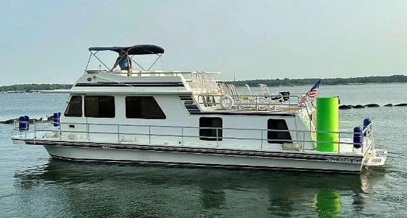 Slide: The Image of 2004 Gibson 50 Houseboat on calm water with upper deck and American flag. - 2
