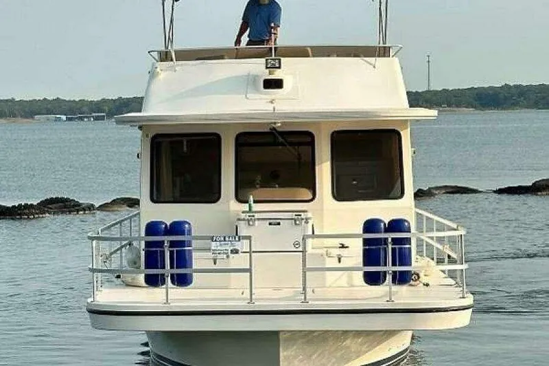 Slide: The Image of 2004 Gibson 50 Houseboat on water, front view, with blue fenders and "For Sale" sign. - 3