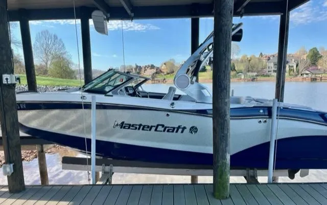 Slide: The Image of 2019 MasterCraft X22 boat docked on a serene lake under a wooden canopy. - 1