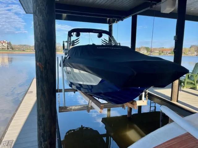 Slide: The Image of 2019 MasterCraft X22 boat covered and docked on a lift by a serene lake. - 12