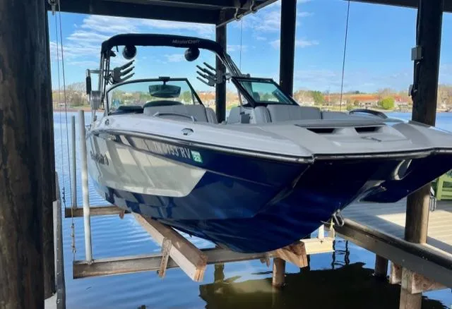Slide: The Image of 2019 MasterCraft X22 boat on lift, docked by a serene lake. - 2