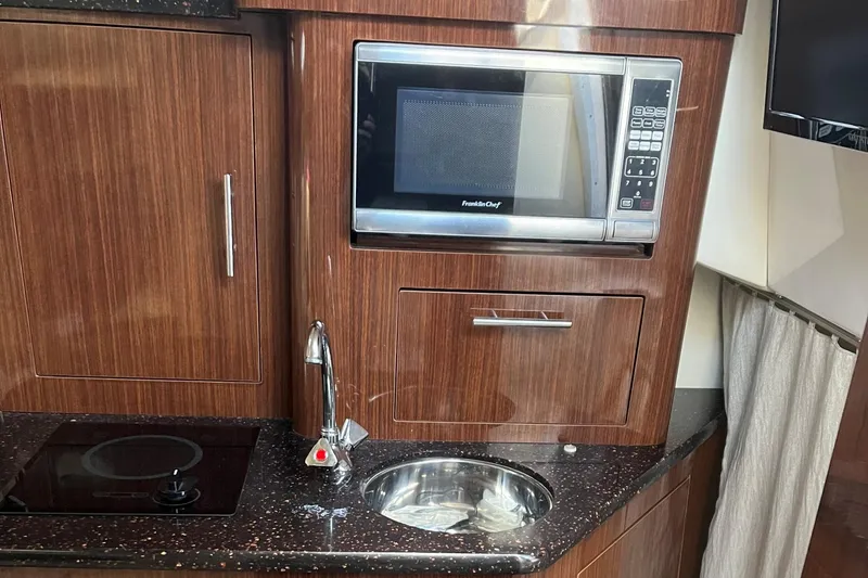 Slide: The Image of 2014 Regal 28 Express boat kitchen with microwave, sink, and stovetop. - 11