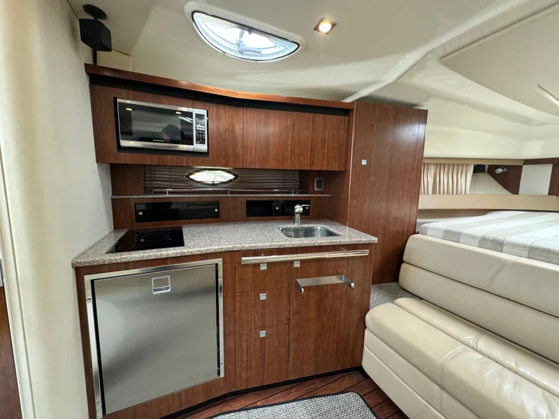 Slide: The Image of 2014 Monterey 340 Sport Yacht interior with kitchenette, featuring wood cabinetry, microwave, and compact fridge. - 13