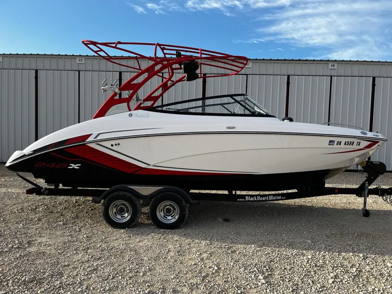Slide: The Image of 2018 Yamaha Boats 242X E-Series on trailer, white and red design, parked outdoors. - 0