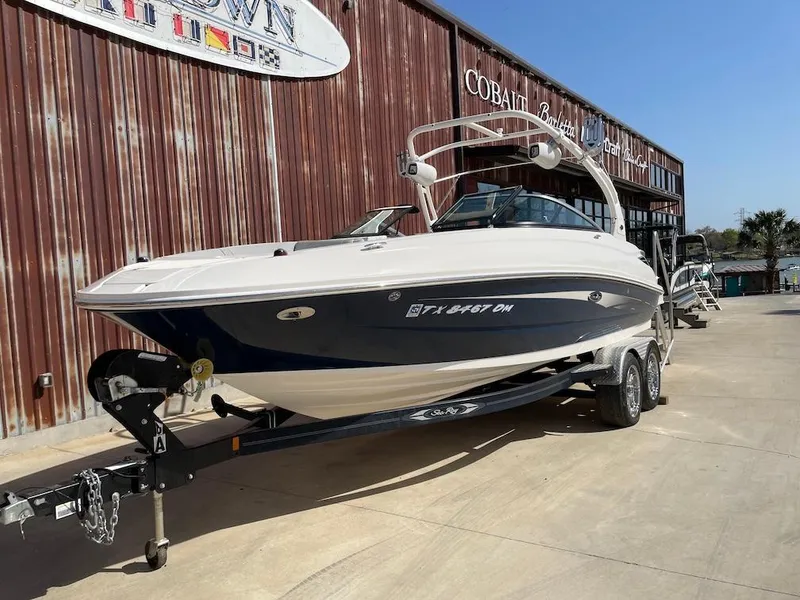Slide: The Image of 2016 Sea Ray 240 Sundeck boat on trailer, parked outside a rustic building. - 1
