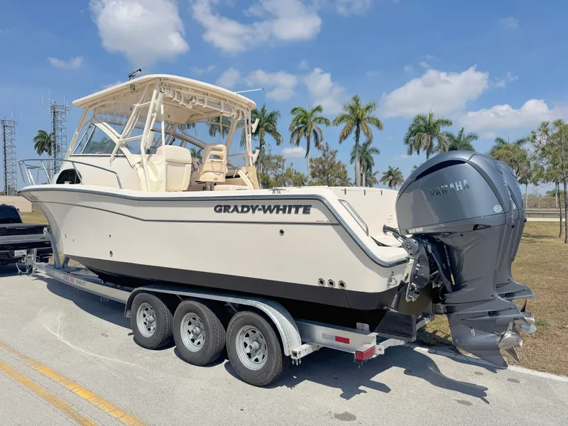 Slide: The Image of 2022 Grady-White Marlin 300 boat on trailer, parked under clear sky with palm trees. - 2