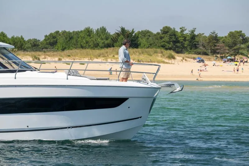 Slide: The Image of 2025 Jeanneau NC 1295 Coupe yacht near a sandy beach with trees in the background. - 11
