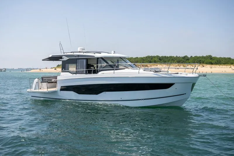 Slide: The Image of 2025 Jeanneau NC 1295 Coupe yacht on calm water near a sandy beach. - 19