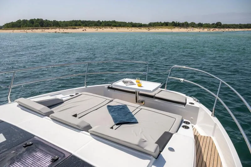 Slide: The Image of 2025 Jeanneau NC 1295 Coupe yacht with sunbathing deck, anchored near a sandy beach. - 22
