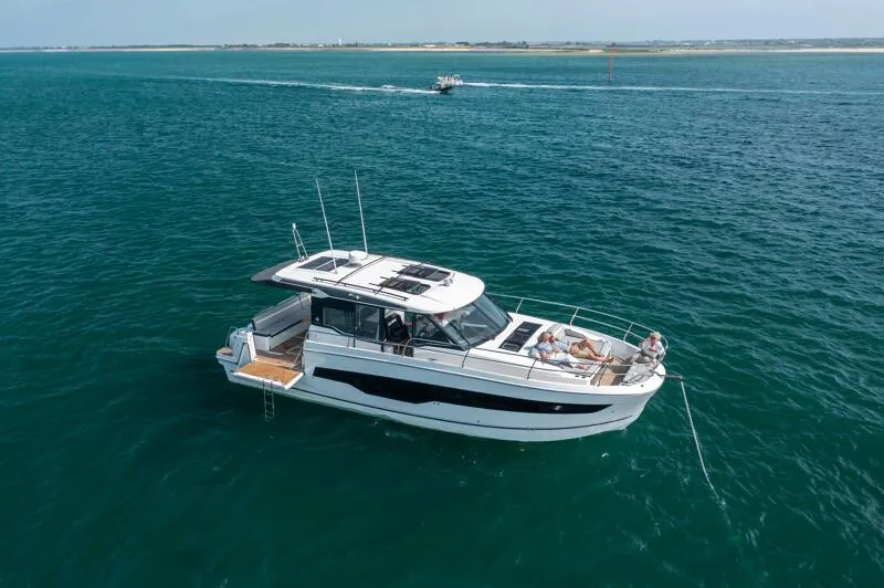 Slide: The Image of 2025 Jeanneau NC 1295 Coupe cruising on open water, with passengers relaxing on deck. - 24